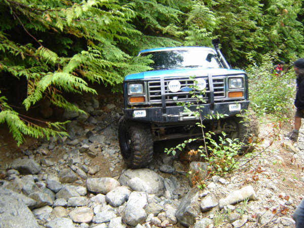 Blue Ford Bronco off-roading on a rocky, wooded trail.