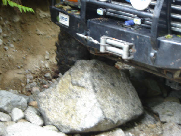 Off-road vehicle with a large rock stuck under its front tire and bumper.