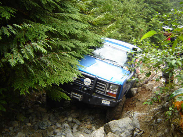 Blue off-road vehicle on a rocky, wooded trail.