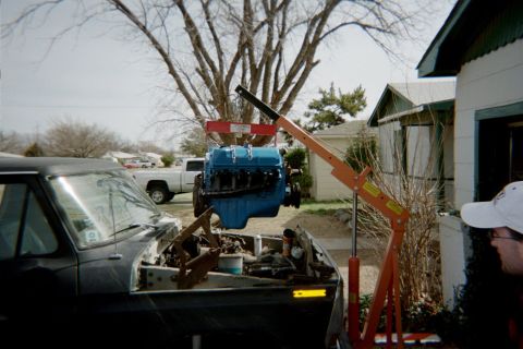 1978 Ford Bronco - A blue engine is being removed from a black truck using an engine hoist.
