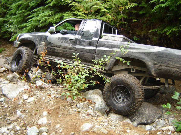 Black pickup truck off-roading on a rocky trail with trees in the background.