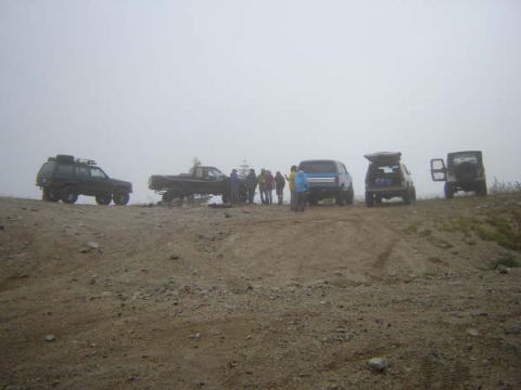 1985 Ford Bronco - A group of people stand around several off-road vehicles on a dirt road with a foggy background.
