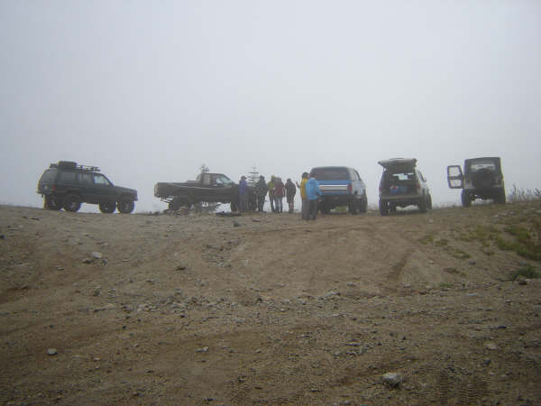 Several off-road vehicles and people on a dirt road in foggy conditions.