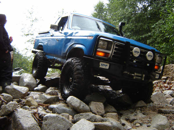 Lifted blue Ford Bronco driving over rocks on an off-road trail.