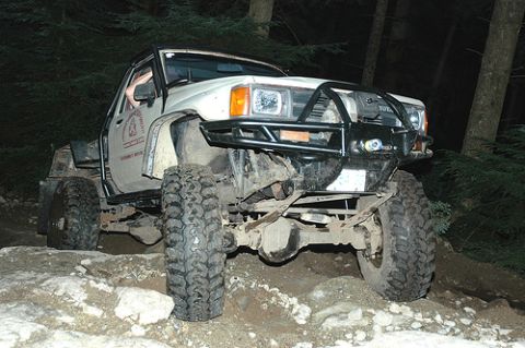 1985 Ford Bronco - A heavily modified white Toyota pickup truck with large off-road tires navigates a rocky trail at night. The truck features a custom front…