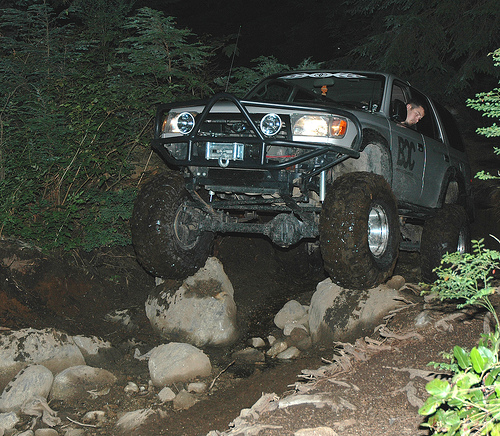 Silver SUV with off-road tires on a rocky trail at night.