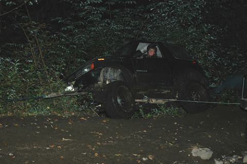 1985 Ford Bronco - A black SUV is being pulled out of a ditch by a winch cable at night. The vehicle is surrounded by trees and brush, and the ground is muddy.