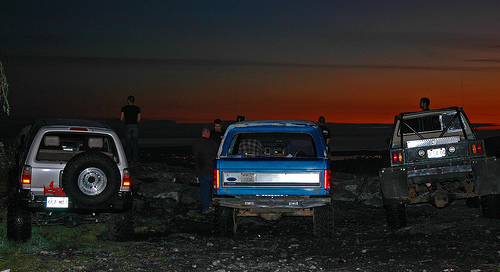Three off-road vehicles parked at dusk with a sunset.