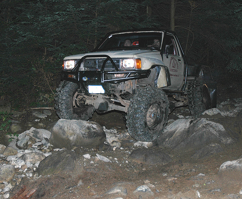 Lifted pickup truck with large off-road tires on a rocky trail at night.