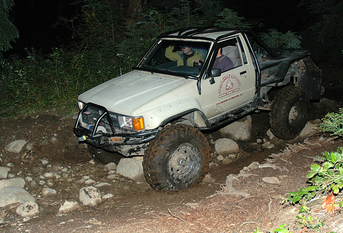 Lifted white pickup truck off-roading on a rocky trail at night.