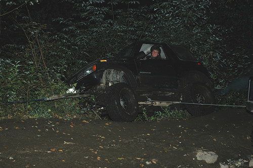 Black off-road vehicle being winched at night in a wooded area.