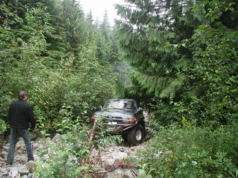 Dark SUV with custom bumper on a rocky trail surrounded by trees.