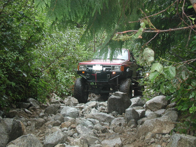 Red 4x4 off-road vehicle on a rocky trail surrounded by trees.