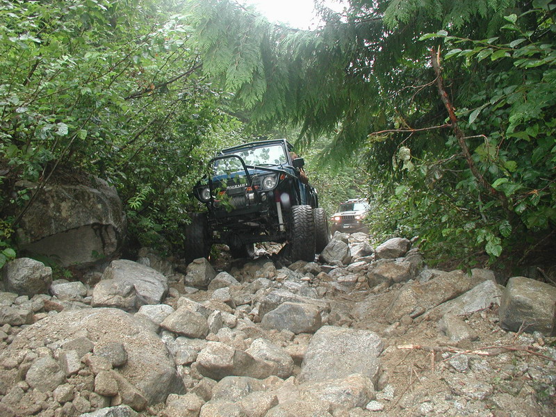 Suzuki Samurai driving on a rocky forest trail.