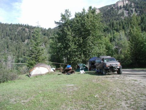 1985 Ford Bronco - A brown SUV is parked at a campsite next to two tents and a picnic table. The vehicle is facing the right side of the frame with its doors…