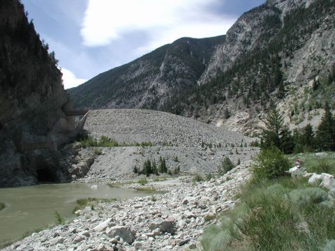 1985 Ford Bronco - A wide river flows through a rocky mountain pass with a tunnel entrance visible on the left. A large, rocky slope dominates the background.