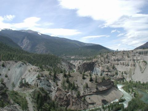 1985 Ford Bronco - A wide shot of a river flowing through a canyon with steep, eroded cliffs and forested mountains in the background.