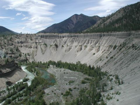 1985 Ford Bronco - A wide shot of a river flowing through a canyon with steep, eroded walls and scattered trees. The sky is partly cloudy.