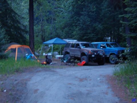 Two off-road SUVs parked at a campsite with a tent and campfire.