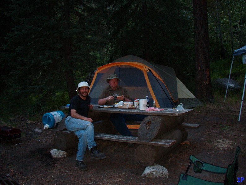Two men at a picnic table in a campsite with a tent.