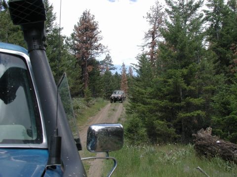 Blue SUV with snorkel driving on a dirt road in a forest, with another SUV ahead.