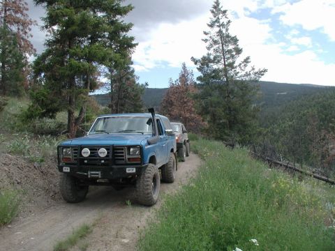 Blue 1980s Ford Bronco with snorkel and brush guard on a dirt road.