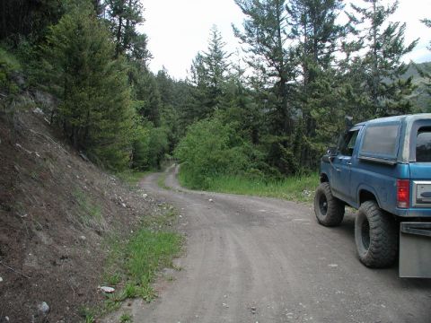Blue Ford Bronco with large tires and snorkel on a dirt road.