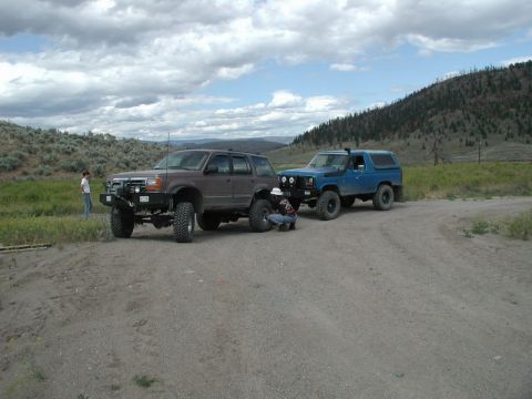 Blue 1985 Ford Bronco with lifted suspension and off-road tires, parked on a dirt road.