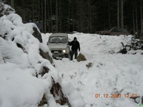 White Suzuki Samurai driving through snow with a person standing nearby.