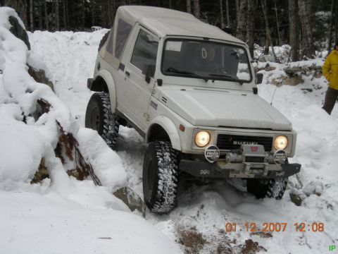 White Suzuki Samurai off-roading in snow with winch and Hella lights