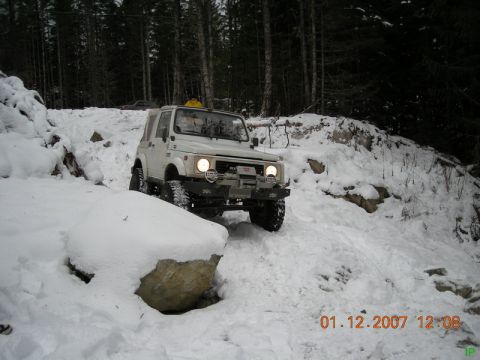 White Suzuki Samurai driving on a snowy, wooded trail.