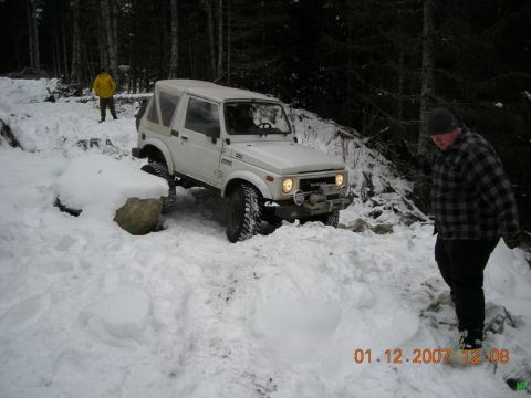 White Suzuki Samurai in the snow with two people nearby.