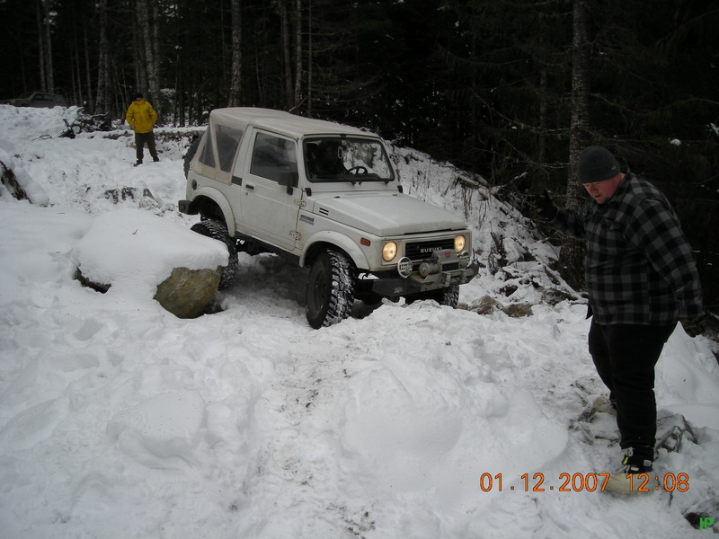 White Suzuki Samurai in the snow with two people nearby.