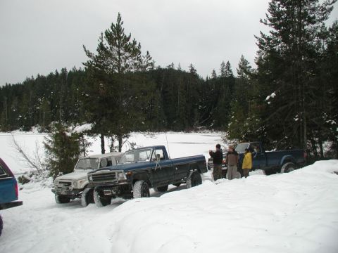 Several off-road vehicles parked in the snow with people standing around them.