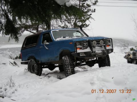 Lifted blue Ford Bronco in the snow with a bull bar.