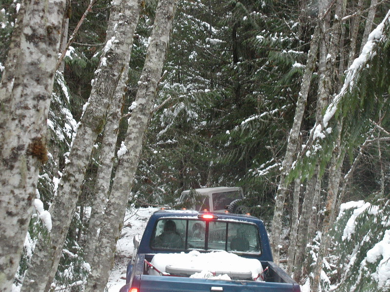 Blue pickup truck and white SUV on a snowy forest road.