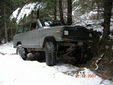 Lifted gray SUV with off-road tires on a snowy wooded trail.