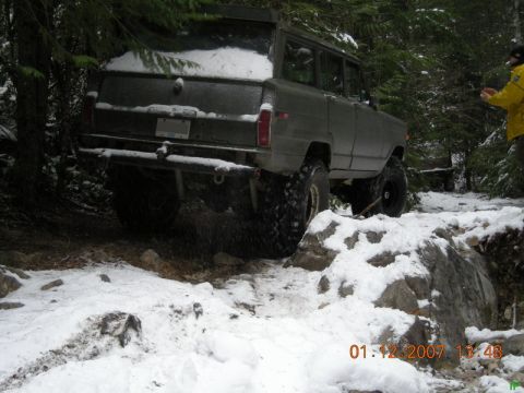 Dark SUV with large tires on a snowy trail in a forest.
