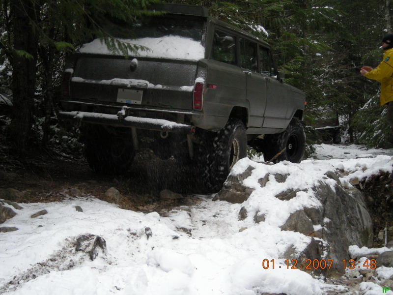 Dark SUV with large tires on a snowy trail in a forest.
