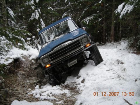 Blue Jeep SUV on a snowy, rocky trail in a forest.