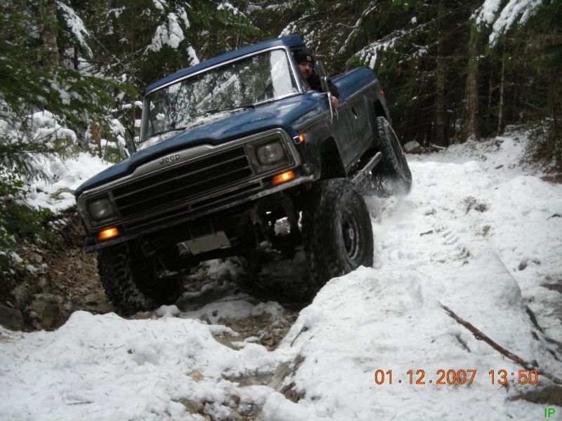 Blue Jeep pickup truck off-roading on a snowy trail in a forest.