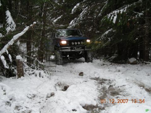 Blue Ford Bronco driving on a snowy forest trail.