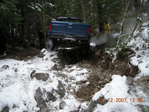 Blue Ford pickup truck on a rocky, snow-covered trail in the woods.
