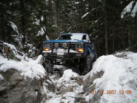 Blue Ford Bronco off-roading through a snowy forest trail