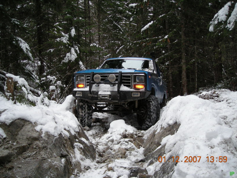 Blue Ford Bronco off-roading through a snowy forest trail