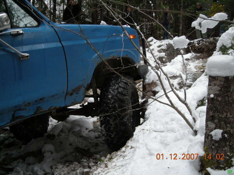 Blue Ford truck with large tires on a snowy trail.