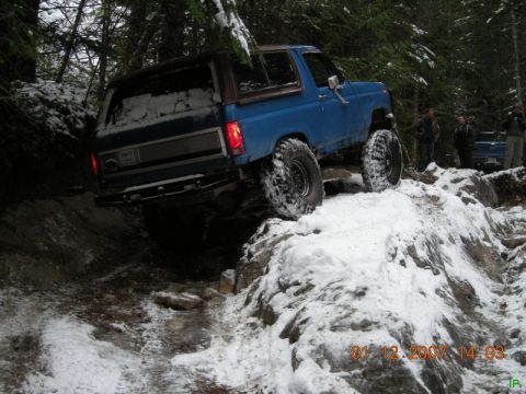 Blue Ford Bronco off-roading on a snowy, rocky trail.