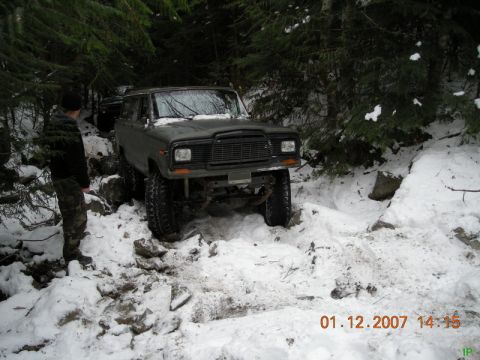 Lifted Jeep Cherokee driving on a snowy, rocky trail in the woods.