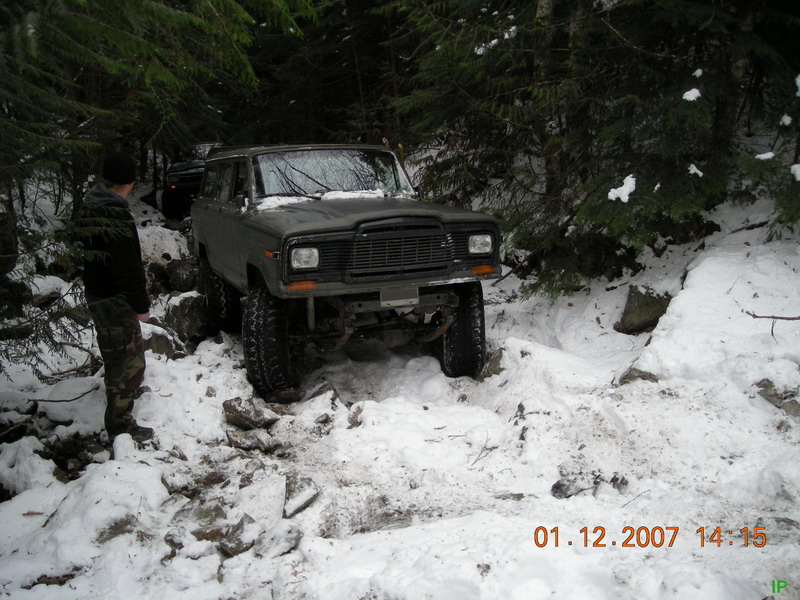 Lifted Jeep Cherokee driving on a snowy, rocky trail in the woods.