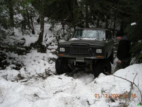Lifted Jeep Cherokee driving through snow in a forest.